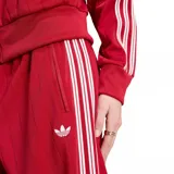 Pantalón deportivo Adidas Firebird Pinstripe de color rojo, con diseño de rayas diplomáticas verticales, corte ancho y pinzas en los laterales. Cuenta con las clásicas tres tiras blancas de la marca en los laterales y el logo del trifolio bordado en la parte frontal. Incluye bolsillos con cierre.