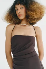 Vestido midi de escote recto con cuello halter y aplicación metálica tipo choker. Presenta frunces laterales en el delantero, abertura en la espalda y cierre con cremallera oculta.
