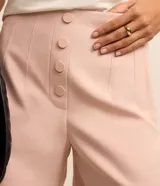 Short de sastrería color rosado, de tiro alto con detalles de pinzas frontales y cartera abotonada con cuatro botones revestidos. Presenta diseño recto y estructurado.