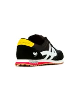 Championes urbanos Hush Puppies en colaboración con Peanuts, color negro con detalles en blanco, amarillo y rojo. Presentan el logo de la marca en el lateral, estampa de Snoopy en el talón y la inscripción Peanuts en la entresuela. Confeccionados en una combinación de gamuza y tela, con suela de goma.