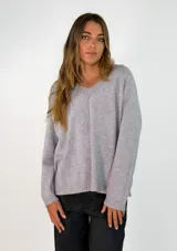 Sweater de punto con escote en V, manga larga y corte holgado. Presenta un diseño liso con costura central vertical en el frente y terminaciones acanaladas en puños y ruedo.