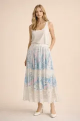 Falda midi de corte evasé, con diseño de paneles que combinan tela estampada en tonos azul y rosado con franjas de encaje blanco en la parte inferior. Presenta cintura elástica y bolsillos laterales.