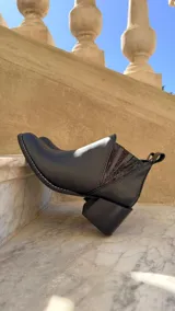 Botinetas de cuero color beige claro con inserciones elásticas laterales en negro y taco cuadrado de madera. Presentan punta fina y tirador trasero.