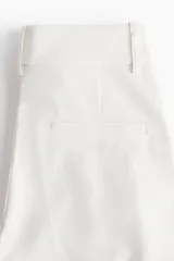 Pantalón sastrero de tiro alto con pinzas, corte holgado y piernas rectas. Presenta cierre frontal con botón y corchete ocultos, bolsillos laterales discretos y bolsillos traseros decorativos.