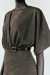 Vestido midi de tejido piqué en color marrón oscuro jaspeado, con escote en pico cruzado y mangas cortas. Presenta detalle de frunces en la cintura y un cinturón integrado con hebilla metálica a contraste.