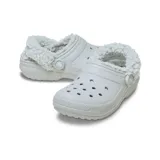 Zuecos Crocs Classic con forro interior de piel sintética tipo sherpa, color gris claro. Presentan el diseño icónico de la marca con perforaciones en la parte superior y correa pivotante en el talón para mayor sujeción.