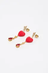 Caravanas colgantes de metal dorado con diseño de flecha decorada con cristales brillantes, un corazón rojo esmaltado y un dije inferior en forma de lágrima con cristal rojo.
