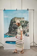 Vestido largo de tejido calado con rayas horizontales en tonos beige, marrón y amarillo. Tiene corte recto, hombros caídos, tajo lateral y logo bordado en la manga.