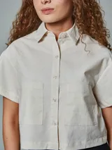 Camisa de lino crudo de manga corta, con cuello camisero, cierre frontal de botones y dos bolsillos aplicados en el pecho.