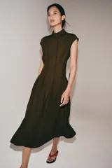 Vestido midi de Zara Woman Collection, confeccionado en mezcla de viscosa y lyocell. Presenta cuello perkins con lazada frontal, diseño sin mangas, pliegues en la cintura y cierre posterior con abertura y botones.