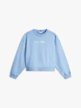 Buzo de felpa celeste Tommy Hilfiger con cuello redondo, manga larga y puños de canalé. Cuenta con el logotipo de la marca bordado en tipografía script en el pecho y detalles de botones dorados decorativos en el hombro.