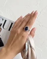 Anillo de plata 925 con piedra central ovalada azul y rodeada de circonias cúbicas en pavé, con banda doble decorada.