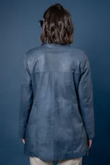 Campera de cuero en tono azul con efecto gastado, de corte recto y largo medio. Presenta cuello camisero, cierre frontal con botones a presión ocultos bajo una solapa y bolsillos laterales con cierre metálico.