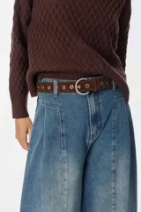 Cinturón de cuero color marrón con hebilla metálica redonda y perforaciones decorativas en forma de flor a lo largo de toda la tira.