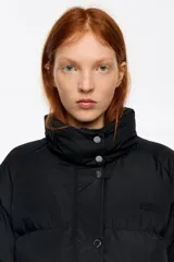 Campera tipo plumífero de largo medio y corte recto en tejido técnico, con cierre frontal, capucha con borde de pelo sintético desmontable y bolsillos frontales con solapa.