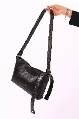 Bandolera de cuero negro con diseño rectangular, caracterizada por una correa ancha decorada con múltiples ojales metálicos y detalles de costuras laterales entrelazadas.