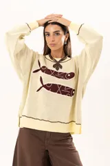 Buzo tejido de punto en color manteca, con diseño frontal de dos sardinas en color bordó. Presenta detalles bordados a mano en los bordes de las figuras y terminaciones con galón picot en cuello, puños y ruedo. Posee un corte holgado y aberturas laterales en el bajo.