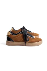 Championes urbanos de gamuza color marrón, con detalles en charol negro y bordes dorados. Presentan cordones negros y suela de goma al tono.