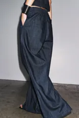Pantalón culotte de denim azul oscuro, tiro medio, con cintura elástica en la parte trasera, bolsillos laterales y pinzas delanteras. Cierre frontal con cremallera, botón y ganchos metálicos.