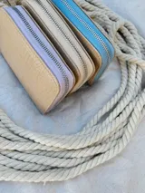 Billetera pequeña de cuero con textura efecto cocodrilo, cierre metálico perimetral y correa de muñeca extraíble. Incluye detalle de moneda metálica decorativa.