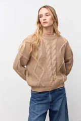 Sweater de punto color camel con cuello redondo y diseño de trenzas verticales en el frente y mangas. Presenta puños y ruedo acanalados.