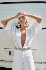 Camisa de lino color blanco con cuello solapa, escote en pico y cierre frontal con botones. Presenta mangas anchas de largo tres cuartos con dobladillo y bajo asimétrico.