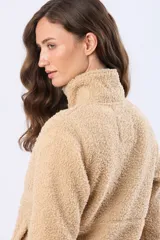 Campera beige de poliéster con textura sherpa, cierre frontal con cremallera marrón y bolsillos laterales.
