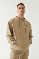 Buzo canguro color arena de felpa, con capucha y cordones ajustables. Tiene puños y cintura acanalados, bolsillo tipo canguro y logo en grifa de plástico.