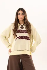 Buzo tejido de punto en color manteca, con diseño frontal de dos sardinas en color bordó. Presenta detalles bordados a mano en los bordes de las figuras y terminaciones con galón picot en cuello, puños y ruedo. Posee un corte holgado y aberturas laterales en el bajo.