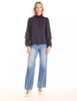 Blusa Tahari de gasa satén color violeta oscuro, con cuello alto fruncido y mangas largas abullonadas. La espalda tiene una abertura central con cierre de botón.