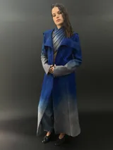 Tapado largo de lana merino color gris oscuro con teñido degradado en gris claro en ruedo, mangas y capucha. Tiene corte recto, bolsillos laterales y cierre cruzado con broches a presión ocultos en los hombros.