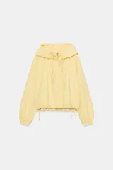Chaqueta de nylon color amarillo pastel, con cuello subido y capucha. Presenta cierre frontal con cremallera, mangas largas con puños elásticos y detalle de lazadas ajustables en el frente. El bajo cuenta con cordón elástico y stoppers para un ajuste personalizado.