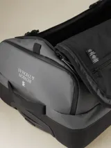 Valija gris con ruedas, manija extensible y correas de ajuste externas.