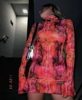 Vestido corto de microtul elastizado con estampado floral en tonos naranja, rosa y negro. Tiene cuello alto y mangas largas acampanadas.