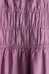 Vestido corto lila con escote cuadrado, mangas cortas abullonadas y fruncido elástico bajo el busto. Presenta volados en el escote, mangas y ruedo.