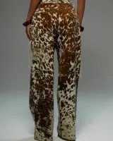 Conjunto de dos piezas con estampado de vaca en tonos marrón y blanco. Incluye un top sin mangas con cuello alto y cierre frontal mediante cordones cruzados, y un pantalón de corte holgado a juego.