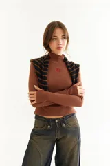 Top de manga larga con cuello alto, confeccionado en tejido de lycra y algodón. Presenta costuras a contratono, bordado central en el pecho, aberturas laterales en el ruedo y diseño con dedal en las mangas.