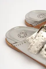 Sandalias de cuero color negro con dos tiras anchas sobre el empeine, cada una con hebillas metálicas ajustables y detalles de tachas plateadas. La suela es de cuero con un borde de color madera.