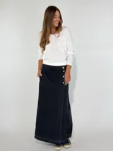 Pollera larga de jean negro con corte evasé, cierre lateral con botones y ruedo desflecado.