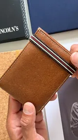 Billetera de cuero color marrón con galón elastizado en colores rojo, verde y blanco. En el interior cuenta con compartimento para billetes, visor y tarjeteros.