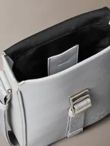 Cartera reporter Calvin Klein color gris, de diseño compacto con solapa frontal y correa ajustable para el hombro. Cuenta con detalles de marca grabados y correa central ajustable.