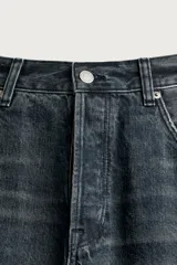 Jeans loose fit de hombre en denim de algodón color gris oscuro con efecto lavado. Presenta perneras con costuras giradas hacia los tobillos, tiro medio, cierre frontal con botones y bolsillos frontales con bolsillo cerillero.