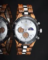 Reloj cronógrafo con caja de madera de zebrano y bisel técnico de acero negro. La esfera es plateada con subdiales de madera, indicador de fase lunar y fechador. La malla combina eslabones de acero inoxidable con madera de zebrano.
