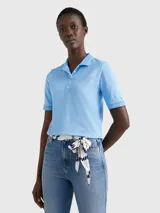 Chomba celeste de piqué de algodón con cuello ribeteado, cartera de cinco botones, logo de Tommy Hilfiger bordado en el pecho y bandera de Tommy Hilfiger bordada en la manga.