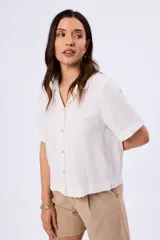 Camisa de manga corta color blanco, confeccionada en mezcla de viscosa, poliamida y lino, con cuello camisero y cierre frontal de botones.