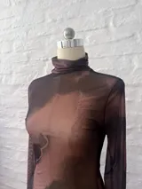 Vestido corto de microtul elastizado en color marrón con efecto degradado. Presenta cuello alto, mangas largas con terminación acampanada y bordes con acabado ondulado.