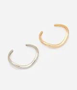 Kit de dos braceletes femeninos de metal reciclado con diseño orgánico, estructura rígida, curvas asimétricas y superficie pulida con efecto espejo, incluyendo una unidad en color dorado y otra en plateado.