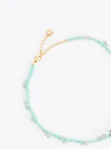 Gargantilla de hilo trenzado color celeste con pequeñas piedras incrustadas a lo largo, cierre de cadena dorada con mosquetón y un dije colgante en forma de corazón marrón con detalles grabados.