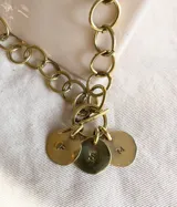 Cadena de eslabones grandes color bronce con cierre tipo toggle y tres dijes redondos con iniciales grabadas.