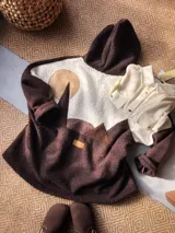Campera tipo hoodie de textura tipo corderito, con diseño de paisaje montañoso en bloques de color marrón, blanco y beige. Presenta capucha y un parche de cuero con logo en la parte posterior.